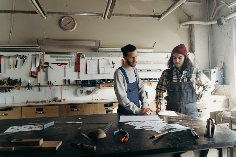 Two craftsmen discussing plans in a well-equipped workshop with tools and blueprints.