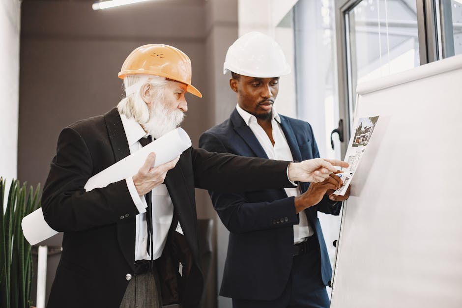 Two architects in suits and hard hats discussing building plans on a whiteboard indoors.