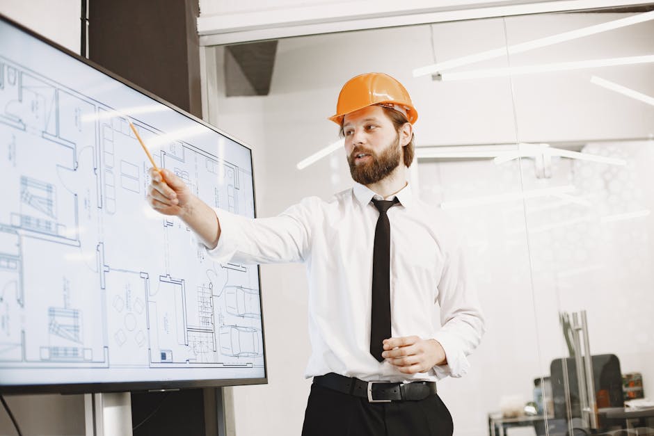 Architect with helmet presenting building blueprints on screen in modern office environment.